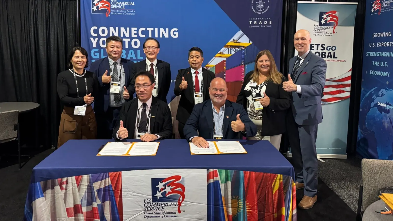 SafeSky Systems USA and Century Minsheng representatives giving a thumbs up behind a table with the signed MOU folders, in front of a U.S. Commercial Service backdrop at AUSA 2026